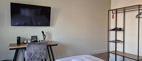 A hotel room with two beds, a desk with a chair, a TV mounted on the wall, and a metal shelf unit.
