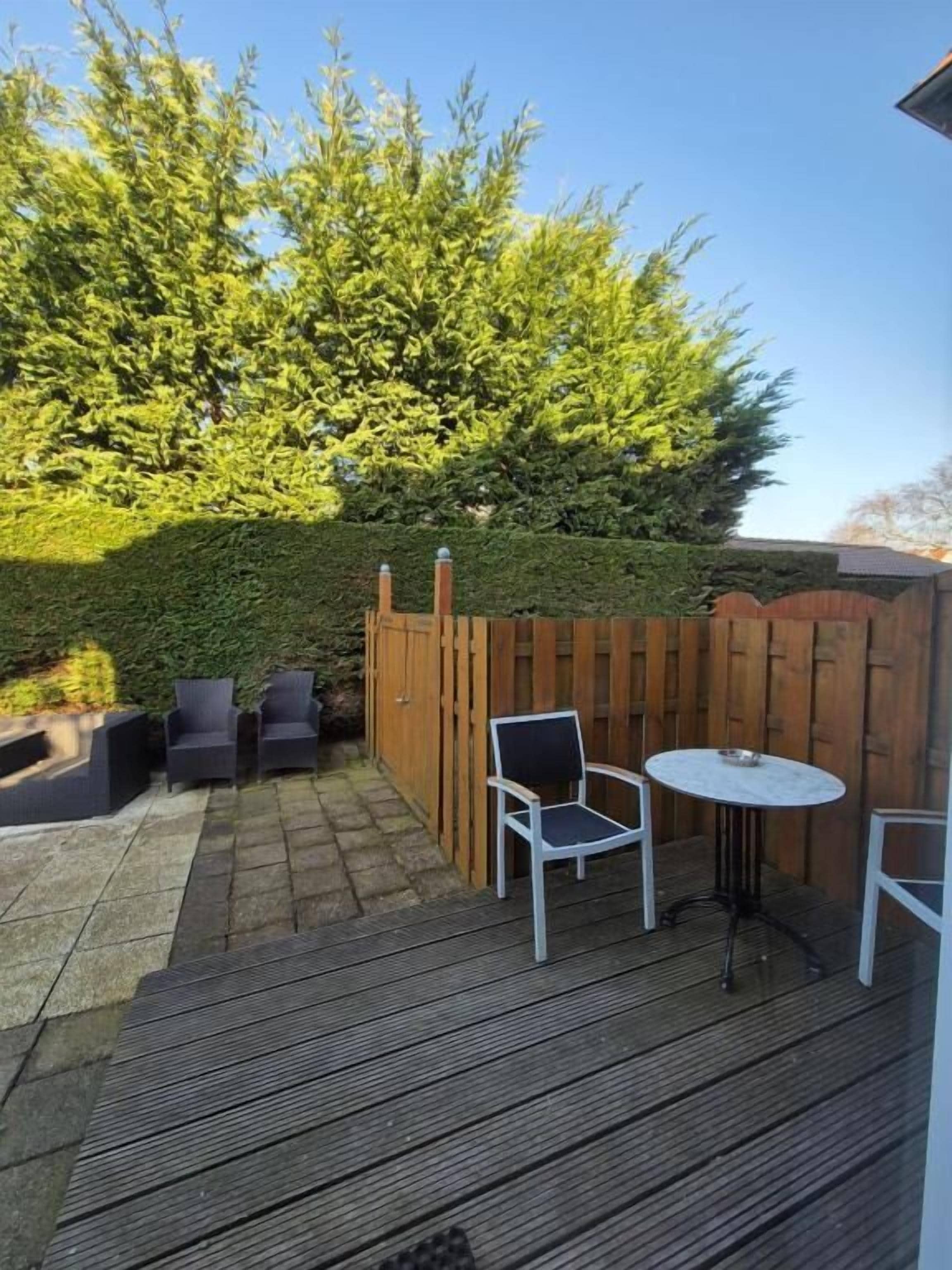 Une terrasse en bois avec des meubles d’extérieur, une haie et une clôture en bois.