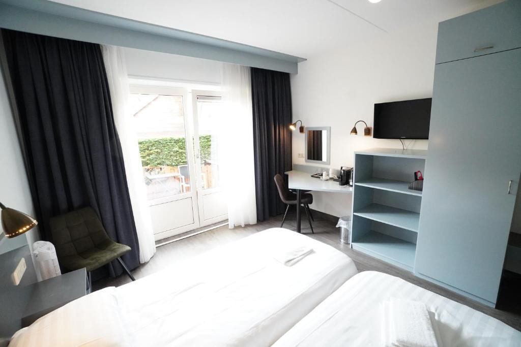 A hotel room with a bed, a desk, a chair, a TV, and a wardrobe.