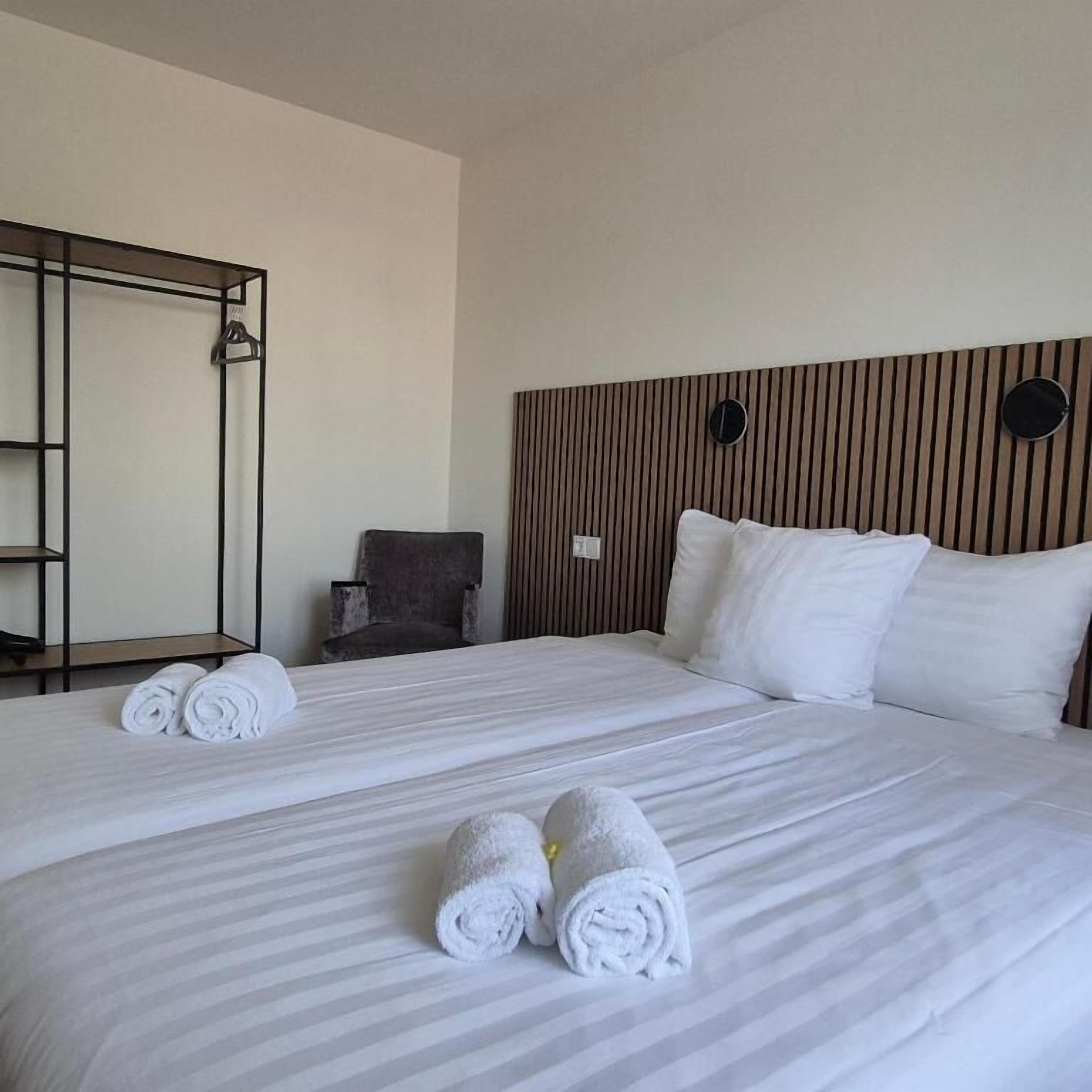 A hotel room with two beds, a wooden headboard, a mirror, a chair, and a wardrobe.