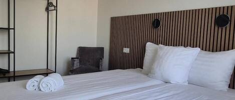 A hotel room with two beds, a wooden headboard, a mirror, a chair, and a wardrobe.