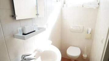 A compact bathroom with a white sink, a mirror, a toilet, and a window above the toilet.