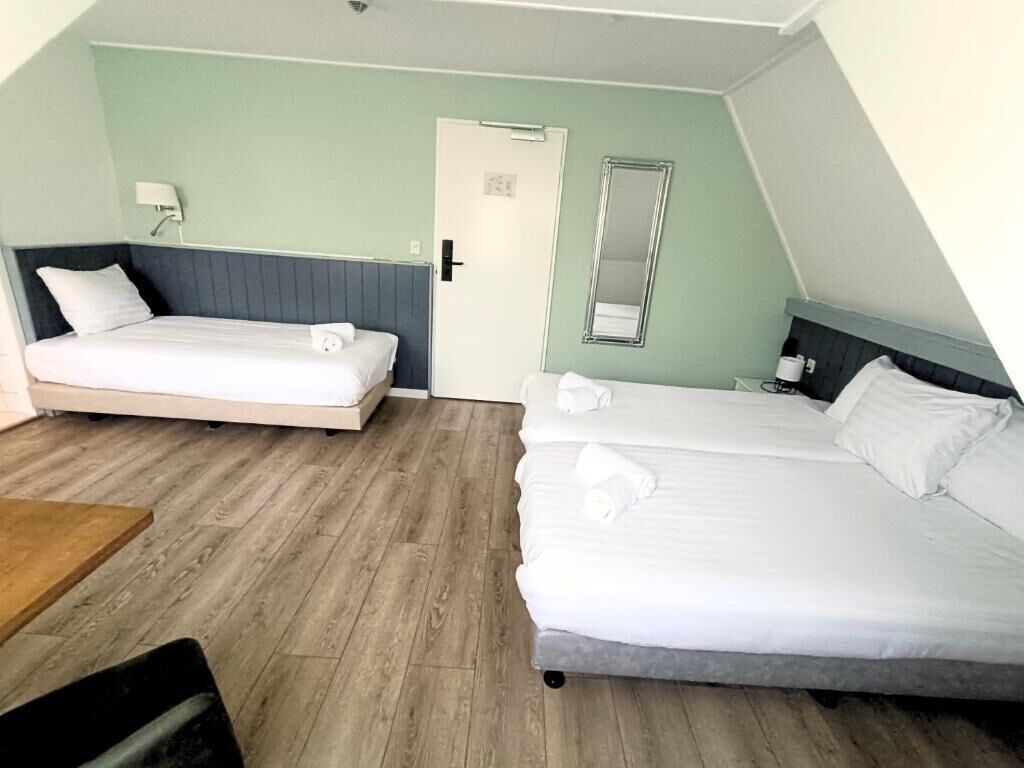 A room with two beds, a wooden floor, a door, a mirror, and a small table.