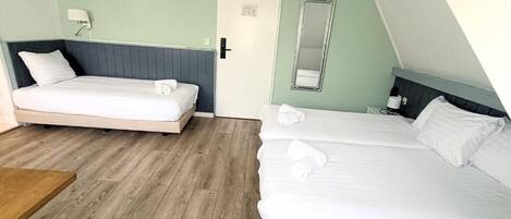 Una habitación con dos camas, piso de madera, una puerta, un espejo y una mesita.