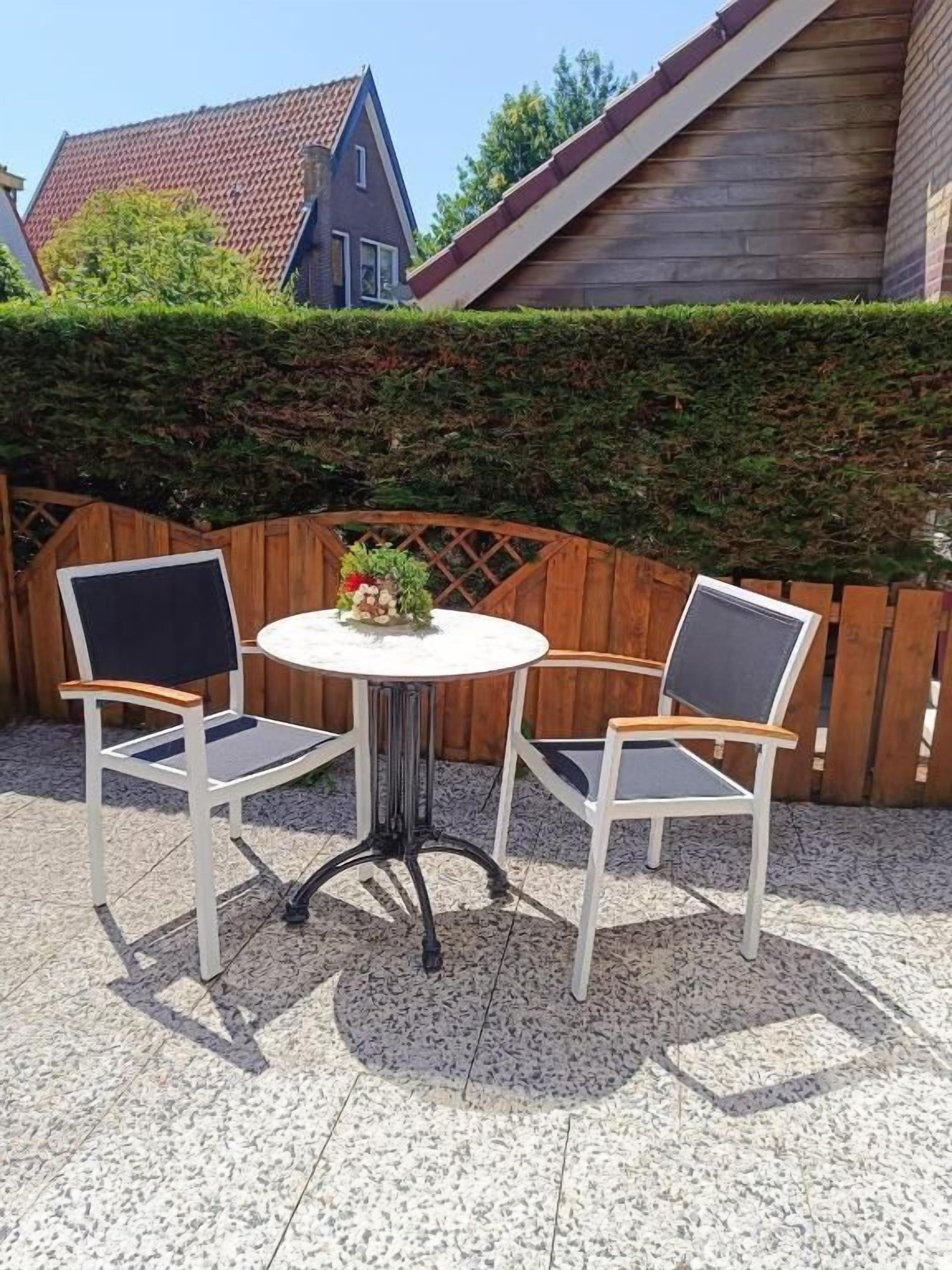 A patio with a round table and two chairs, surrounded by a wooden fence and a hedge.
