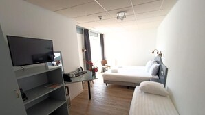 Une chambre d’hôtel moderne équipée d’une télévision à écran plat, d’un canapé-lit, d’un bureau avec une lampe et d’une fenêtre avec des rideaux.