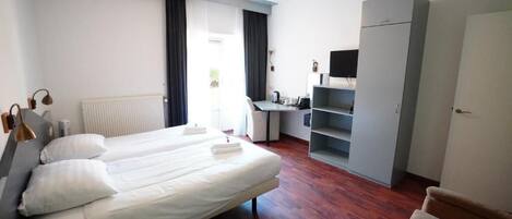 A hotel room with two beds, a desk, a wardrobe, and a chair.