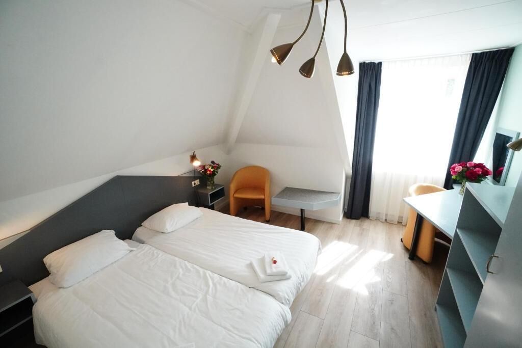 A modern hotel room with two beds, a desk, a chair, and a small table with a vase of flowers.