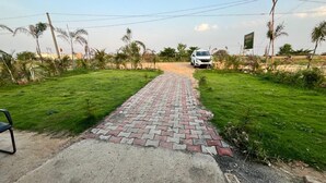 A paved pathway leading to a white car parked in a grassy area with a signboard in the background. - Sunrise Prime (Ranchi)