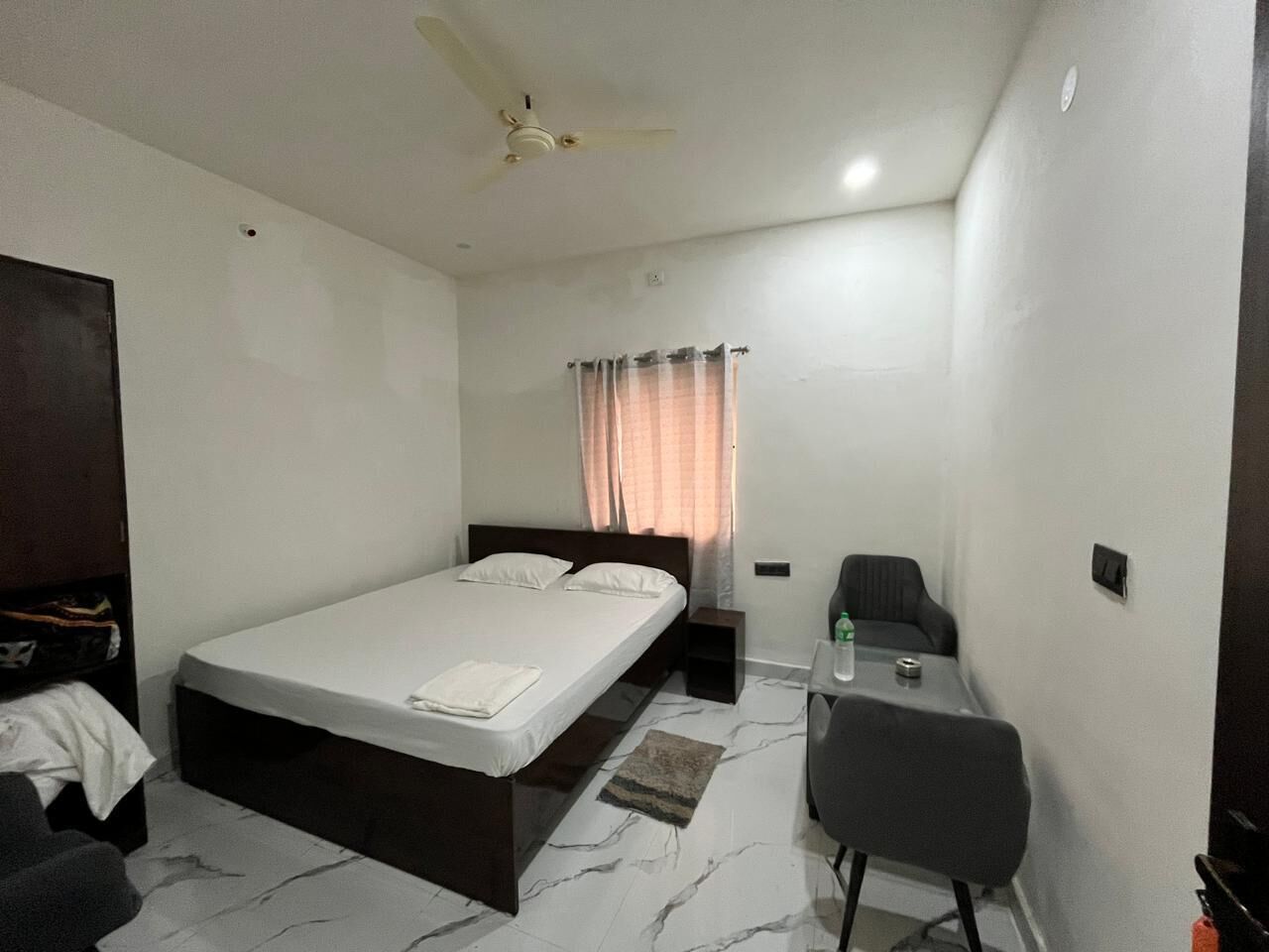 A bedroom with a bed, a desk, a chair, a ceiling fan, and a window with curtains.