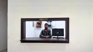 A reception desk with a sign above it, a computer monitor, and a wall-mounted shelf with a small statue. - Sunrise Prime (Ranchi)