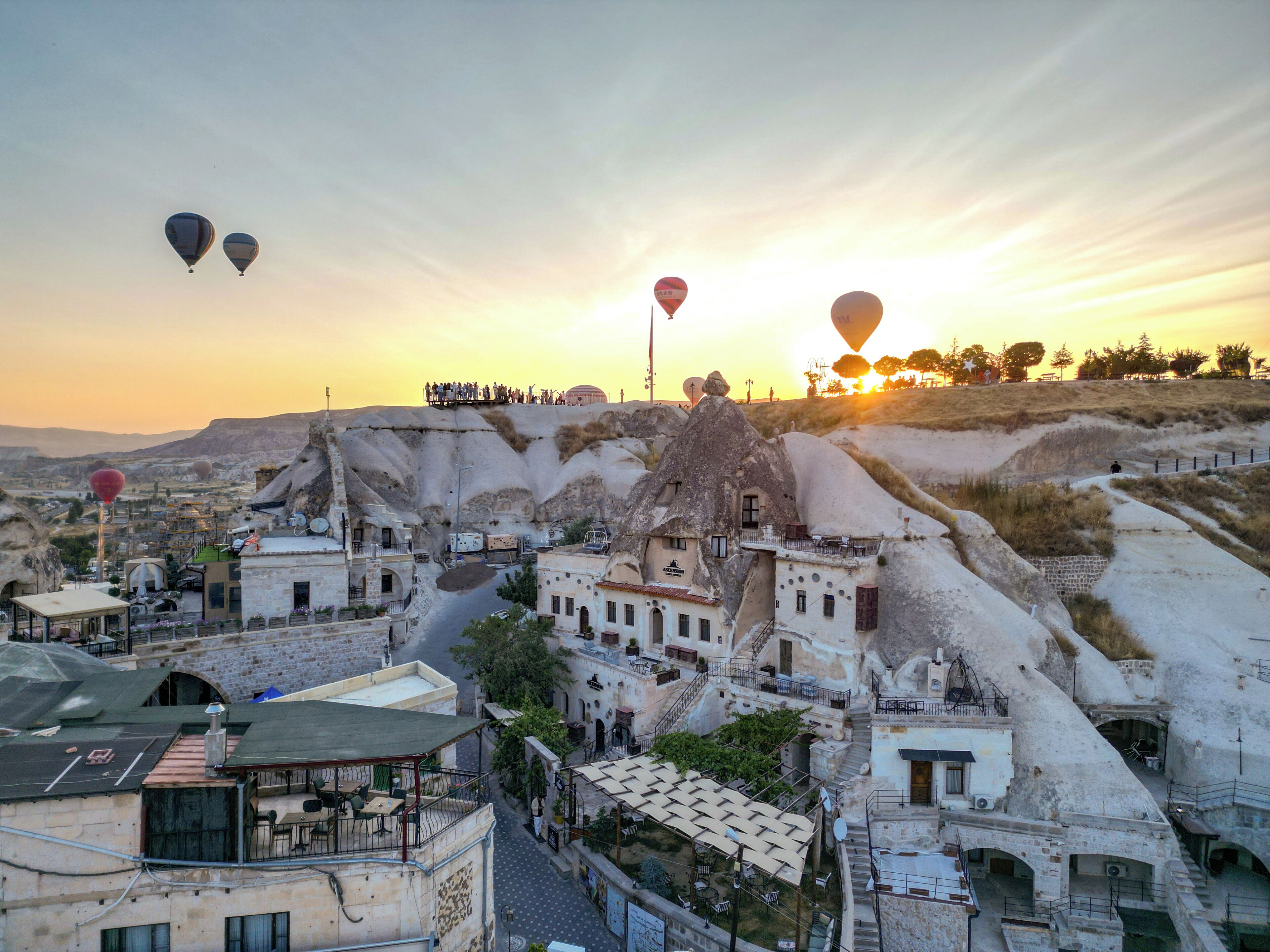 A town with traditional architecture, a street, and hot air balloons in the sky.