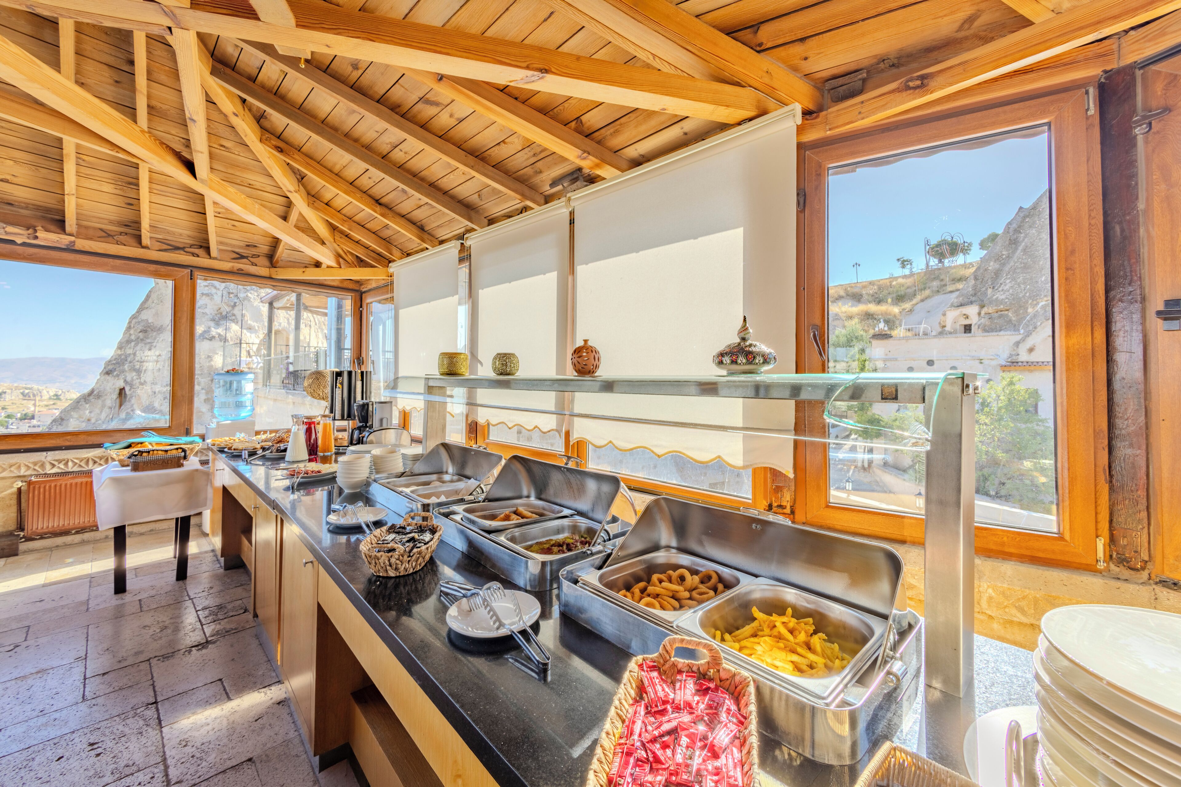 A buffet setup with various food items and utensils, a wooden ceiling, and a view of the outdoors.