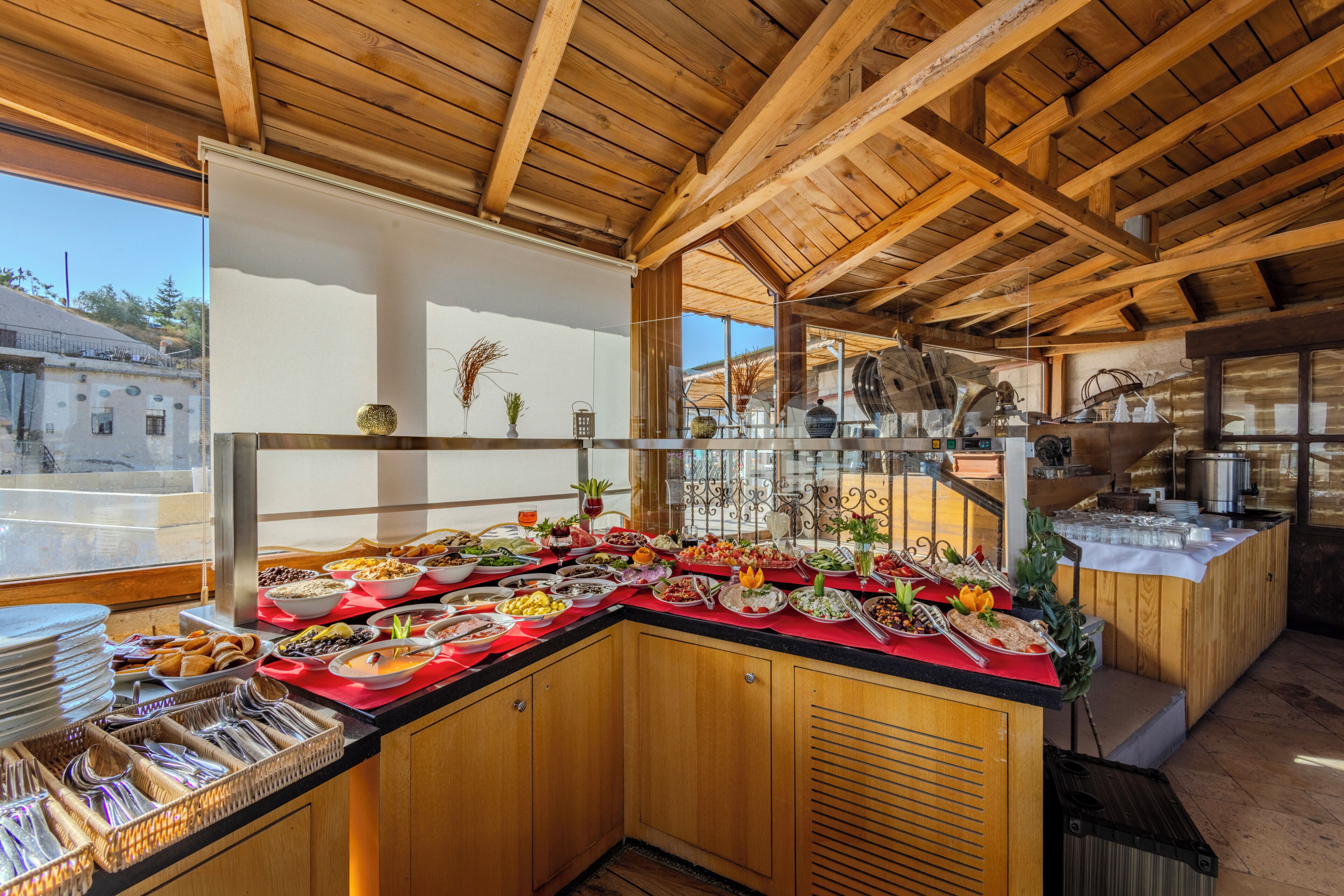 Mostra de buffet amb diferents aliments i utensilis, bigues de sostre de fusta, i vista a l'exterior.
