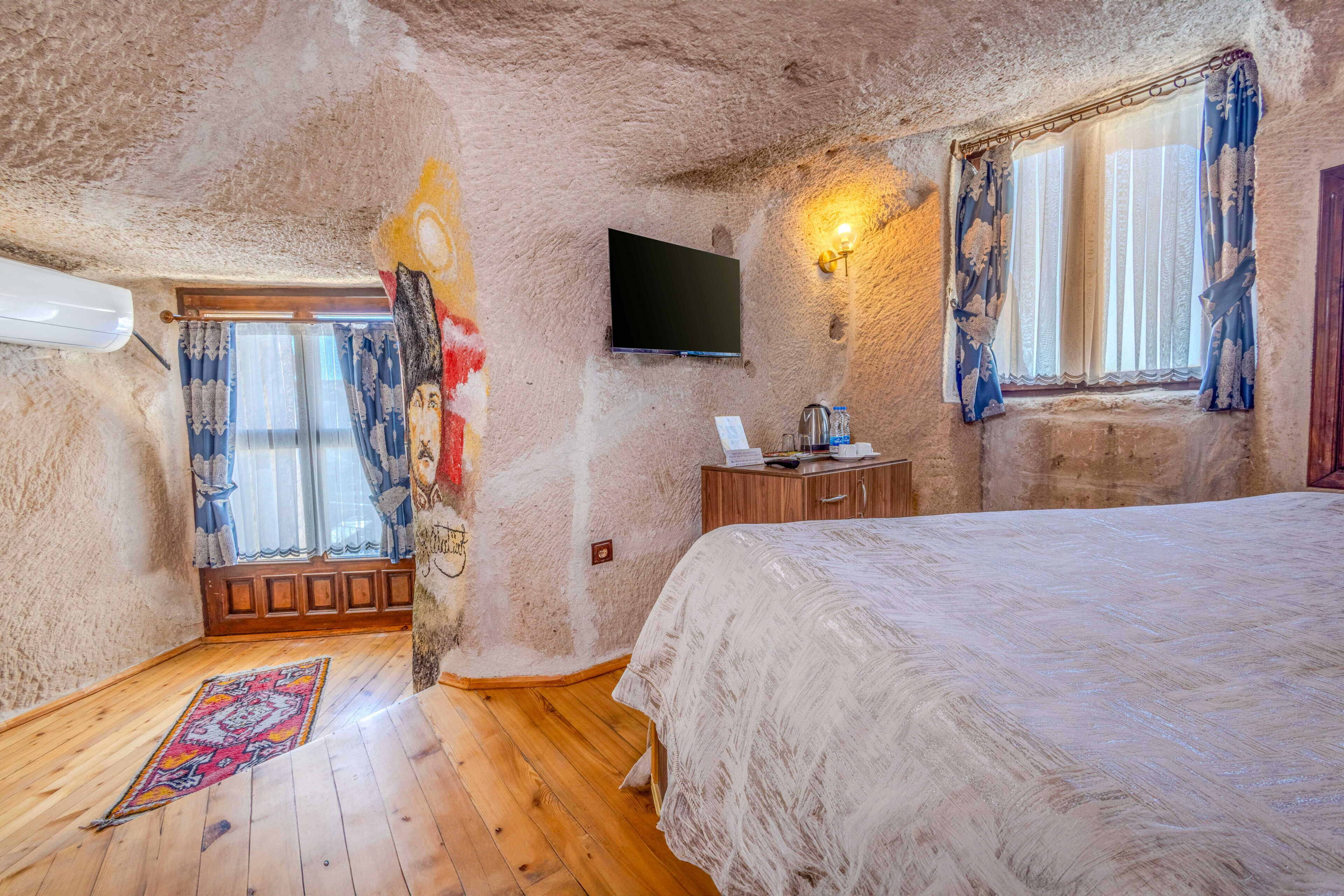 Un dormitorio con cama, televisor, ventana con cortinas y suelo de madera.