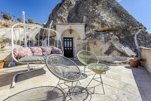 Un patio con una silla colgante, dos sillones de mimbre y un banco con cojines estampados.