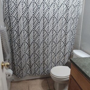 A bathroom with a patterned shower curtain, a toilet, and a sink with a granite countertop. - A Clean, Well-lighted Place:
Tropical Holiday Haven~Where Groove Gets Got Again (Holiday)