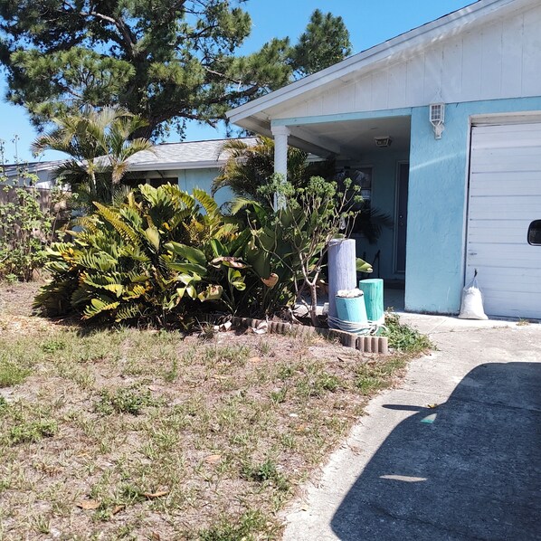 A residential property with a garage, a lawn with various plants, and a clear sky. - A Clean, Well-lighted Place:
Tropical Holiday Haven~Where Groove Gets Got Again (Holiday)