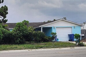 A single-story house with a garage, surrounded by greenery and a clear sky. - A Clean, Well-lighted Place:
Tropical Holiday Haven~Where Groove Gets Got Again (Holiday)