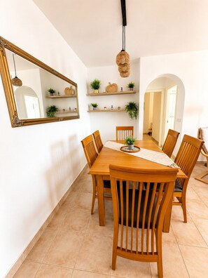 A dining area with a wooden table, six chairs, a large mirror, and shelves with plants. - Seagull Lookout (Mojácar)