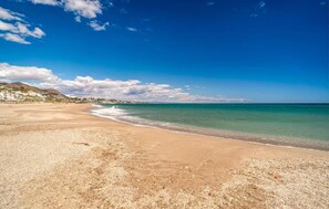 A beach with clear skies, a sandy shore, and distant buildings. - Seagull Lookout (Mojácar)