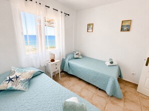 A bedroom with two beds, a nightstand, a lamp, and two paintings on the wall. - Seagull Lookout (Mojácar)