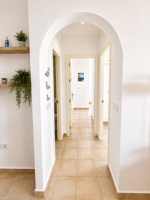 A hallway with a tiled floor, white walls, and an arched doorway. There are potted plants on shelves and a framed picture on the wall. - Seagull Lookout (Mojácar)