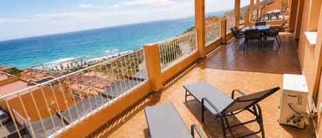 A terrace with a view of the ocean, outdoor furniture, and a pergola.