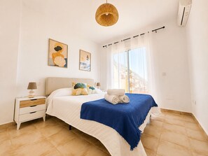 A bedroom with a bed, a nightstand, a lamp, a window with curtains, and artwork on the wall. - Seagull Lookout (Mojácar)
