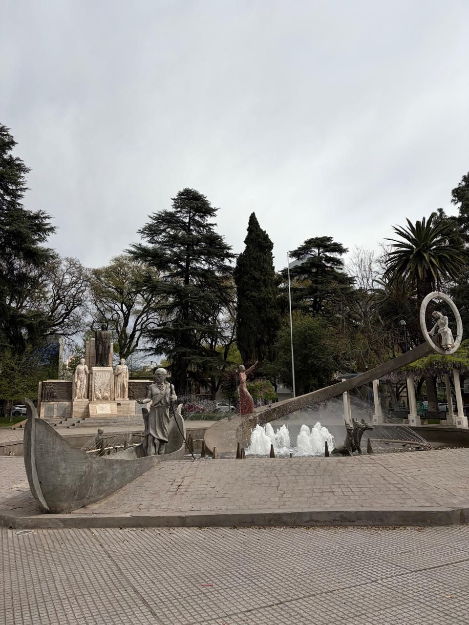Ein Park mit einer Statue, einem Brunnen und einer runden Skulptur.