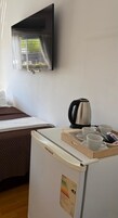 Habitación de hotel con cama, televisor montado en la pared, refrigerador con una bandeja de vasos y una tetera, y una ventana con cortinas.
