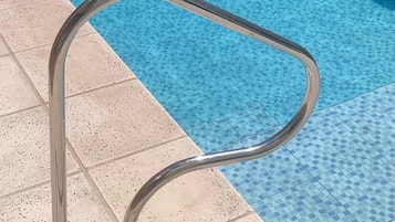 A metal poolside handrail with a curved design, adjacent to a tiled pool area.