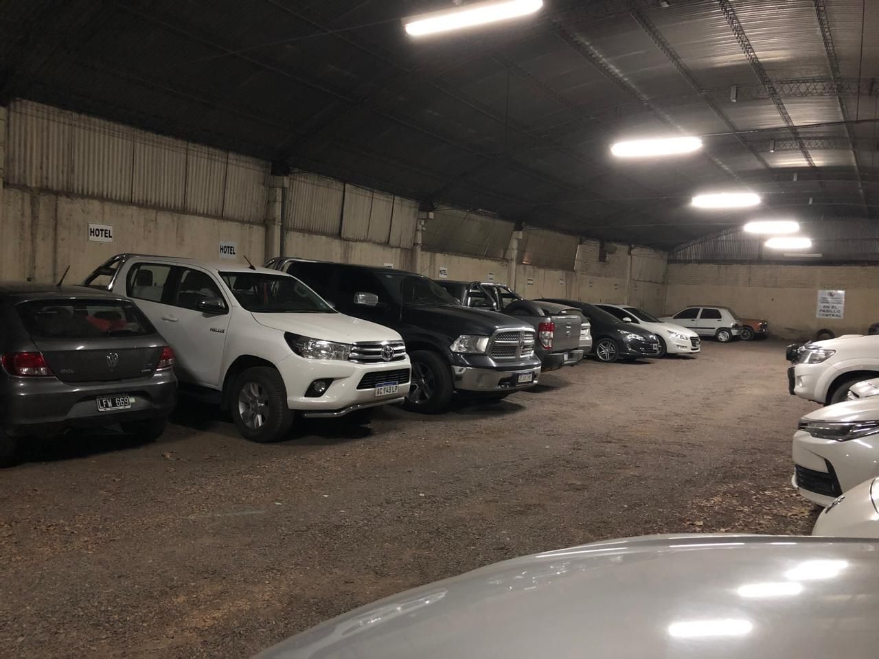 A parking area with multiple cars parked in rows, a concrete floor, and a metal ceiling with fluorescent lighting.
