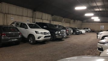 A parking area with multiple cars parked in rows, a concrete floor, and a metal ceiling with fluorescent lighting.