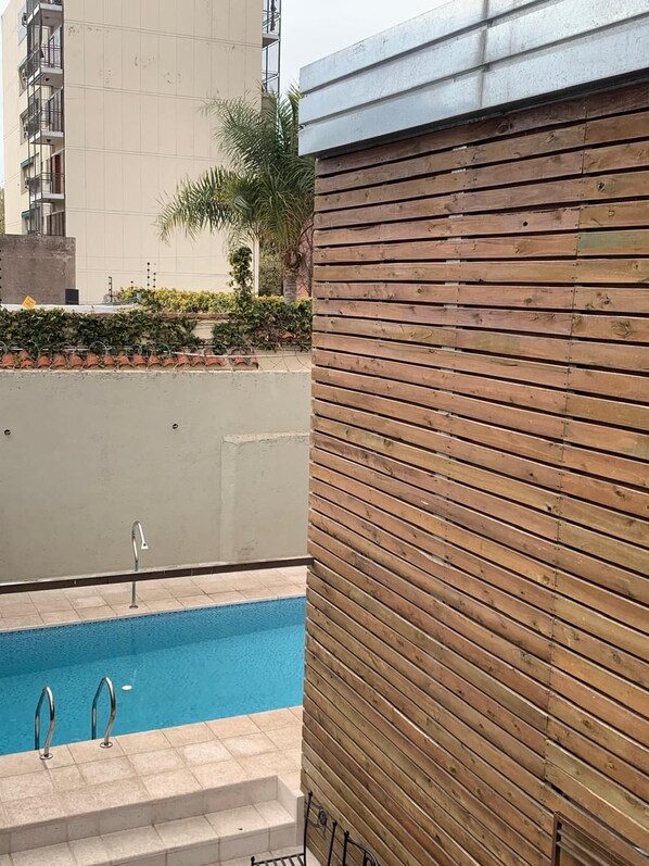 Una piscina con escalones de acceso, rodeada por una valla de madera y un edificio con balcones.