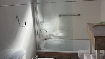 A bathroom with a glass-enclosed shower, a toilet, a bidet, and a sink with a wooden countertop.