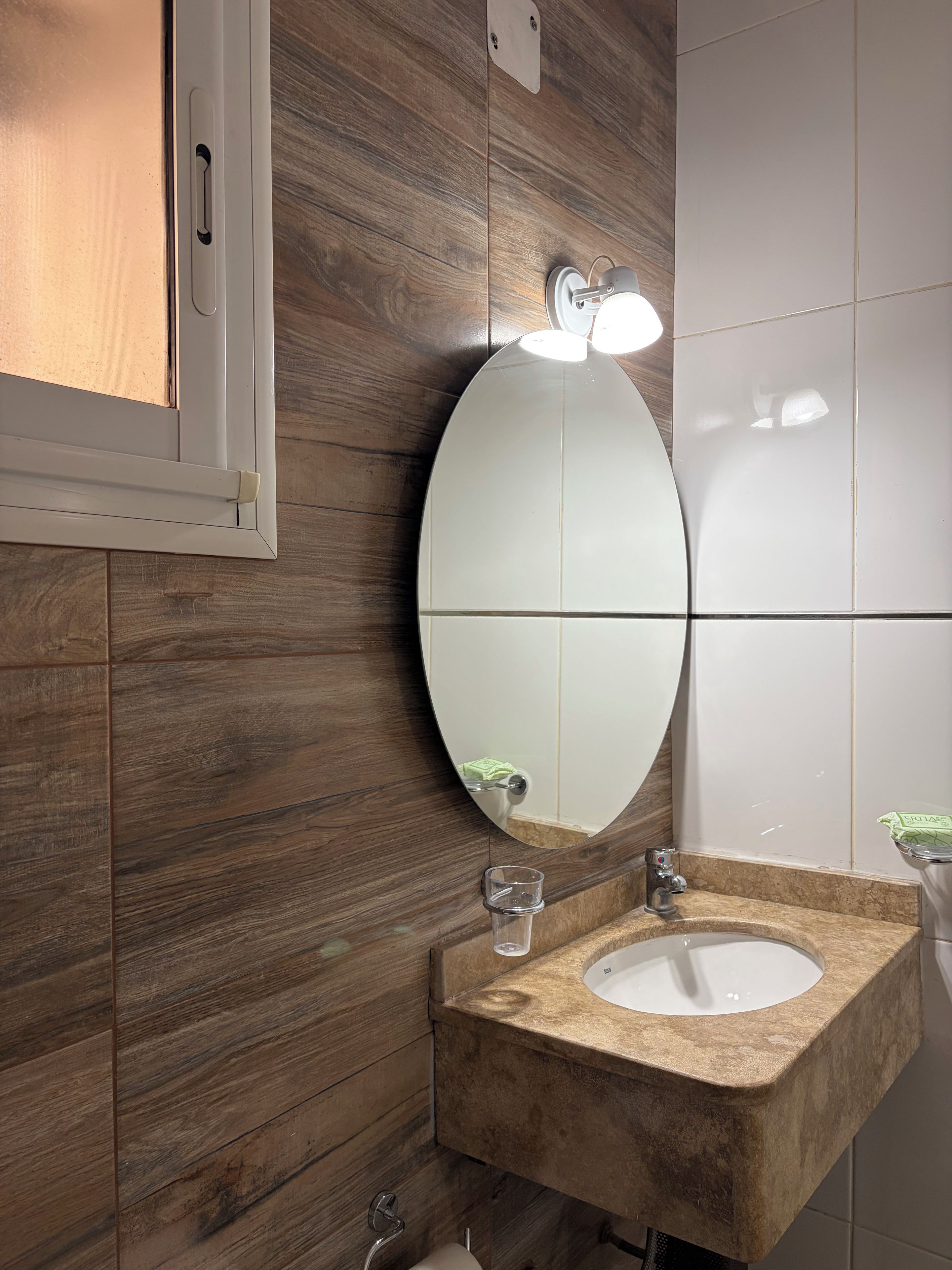 A bathroom with a wooden wall, a white sink, and a mirror.