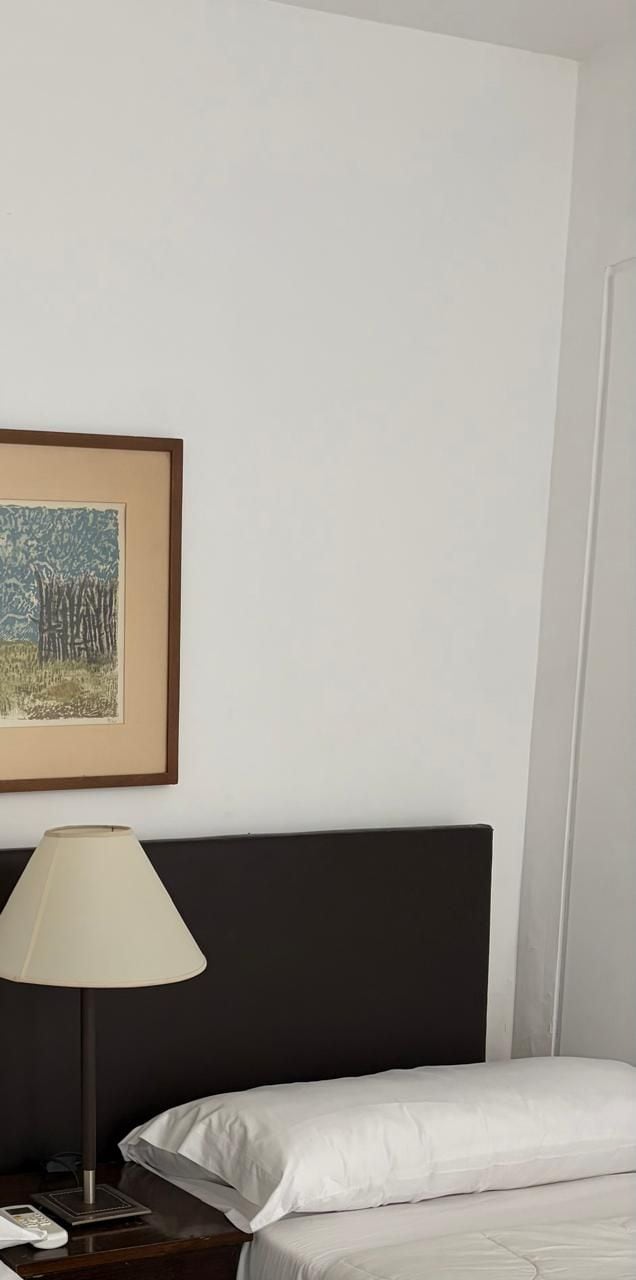 Quarto de hotel com uma cama, mesa de cabeceira, abajur e quadro na parede.