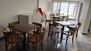 A dining area with multiple tables and chairs, a cabinet, and a large window with blinds. - COLON 737 (Mendoza)