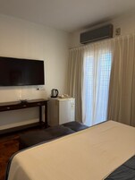 Habitación de hotel con cama, escritorio, televisor de pantalla plana, cafetera y ventana con cortinas.