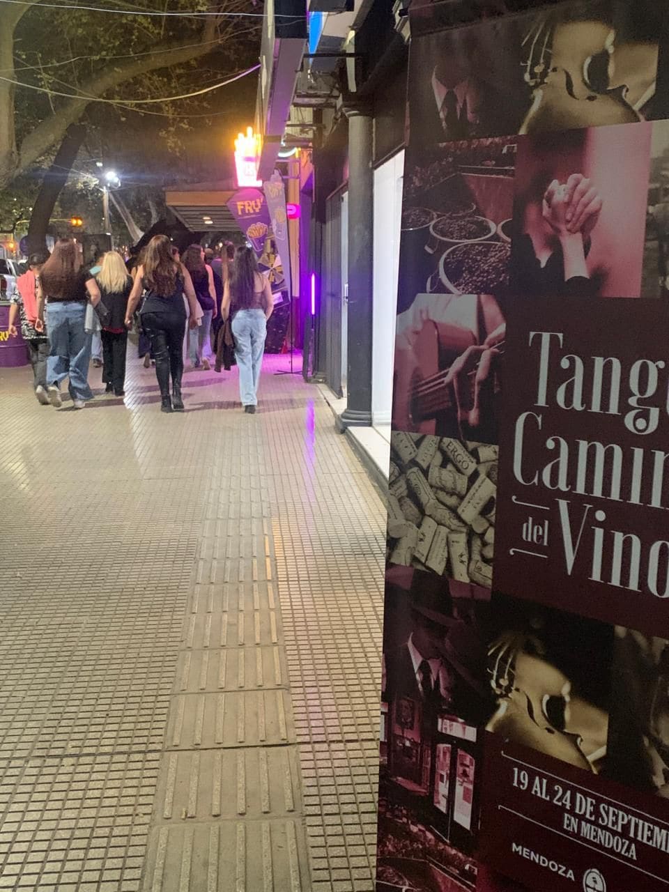 Cena noturna de rua com um cartaz anunciando 'Tang Camilo del Vino'.