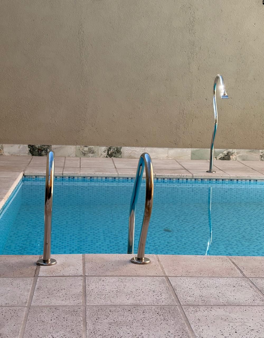 A swimming pool with two metal pool ladders and a tiled deck.