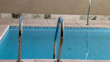A swimming pool with two metal pool ladders and a tiled deck.