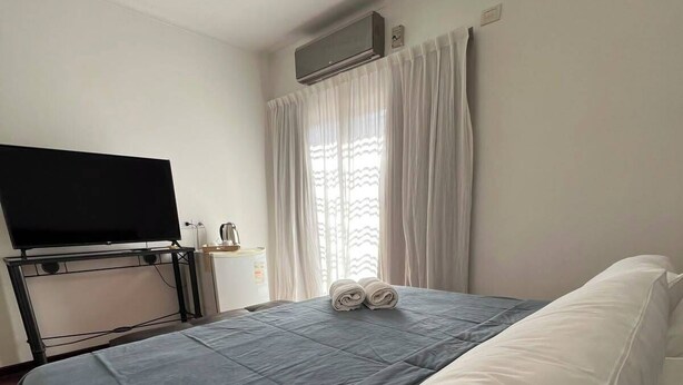 A hotel room with a bed, a flat-screen TV mounted on the wall, a window with curtains, and an air conditioning unit. - COLON 737 (Mendoza)