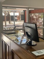 Una mesa de recepción con un monitor de computadora, una mesa de vidrio con una copa de vino y una ventana con vista al exterior.