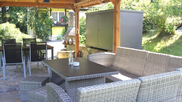 Une terrasse extérieure avec des meubles en osier, une table et un buffet vert.
