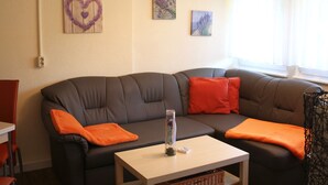 Un salon avec un canapé en cuir foncé, des coussins orange, une petite table sur laquelle est posé un vase, et des œuvres d’art murales.