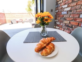 Una mesa redonda cubierta con un mantel blanco, un jarrón con flores amarillas y dos croissants en un plato.