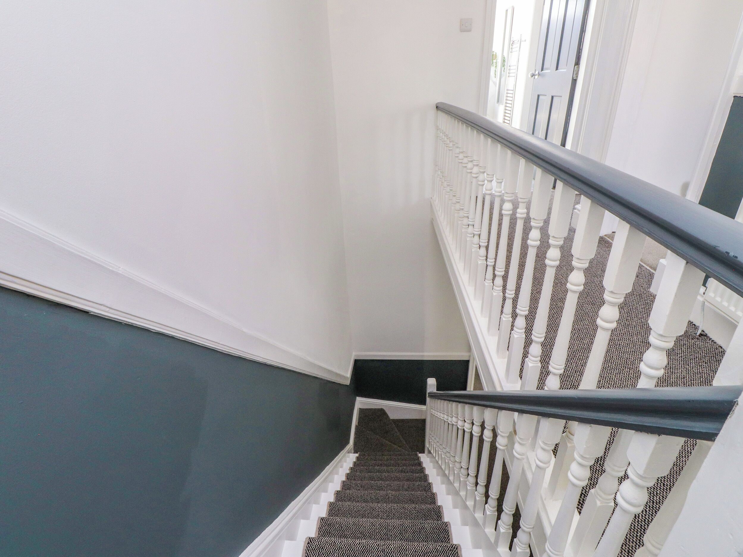 A staircase with white balusters and a black handrail, leading to a door with a white frame.