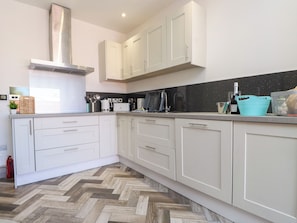 A modern kitchen with white cabinets, a herringbone-patterned floor, and a black backsplash. - Ty Haul (Rhosneigr)